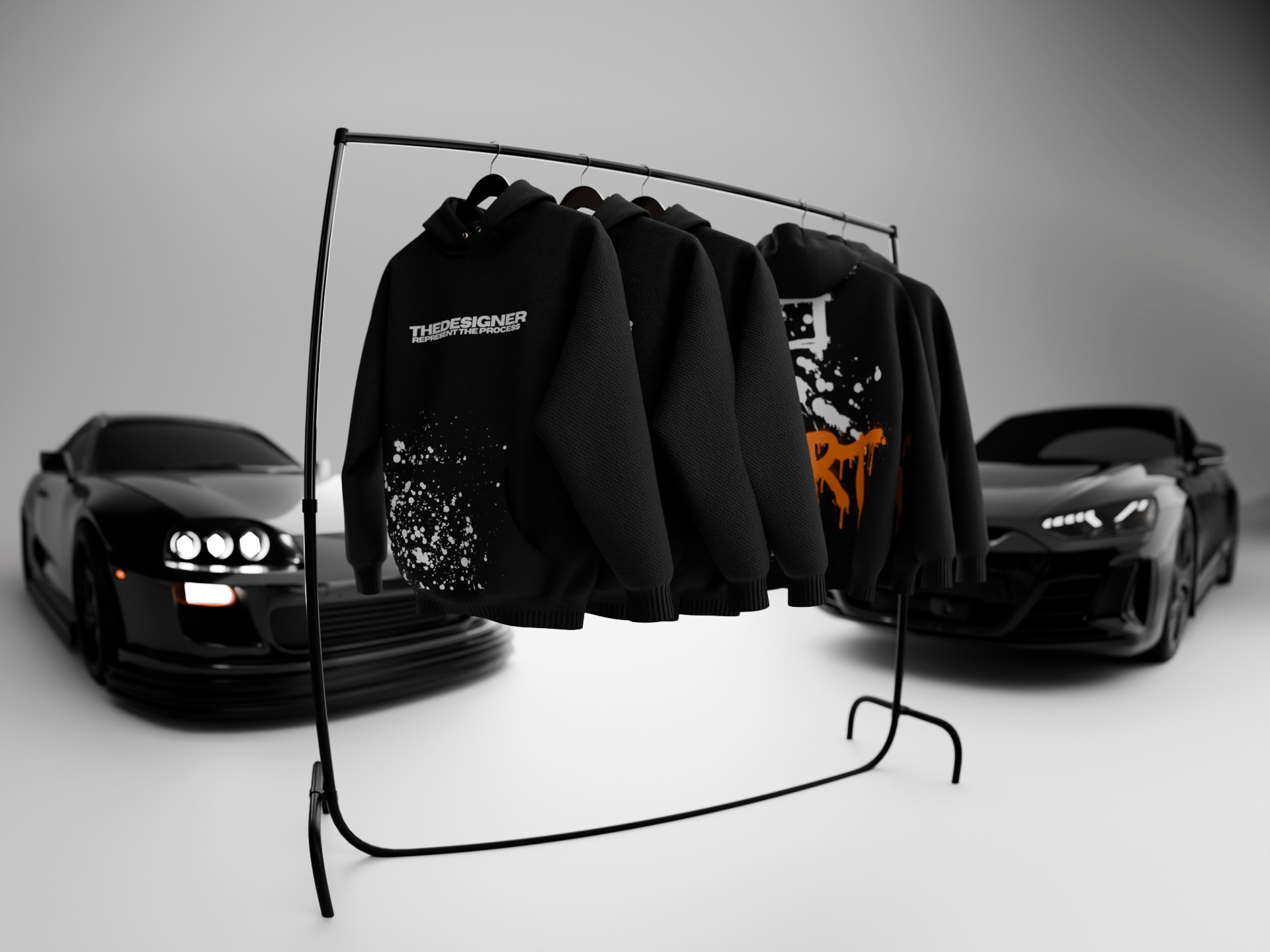Black graphic hoodies on a clothing rack between two black sports cars in a white studio