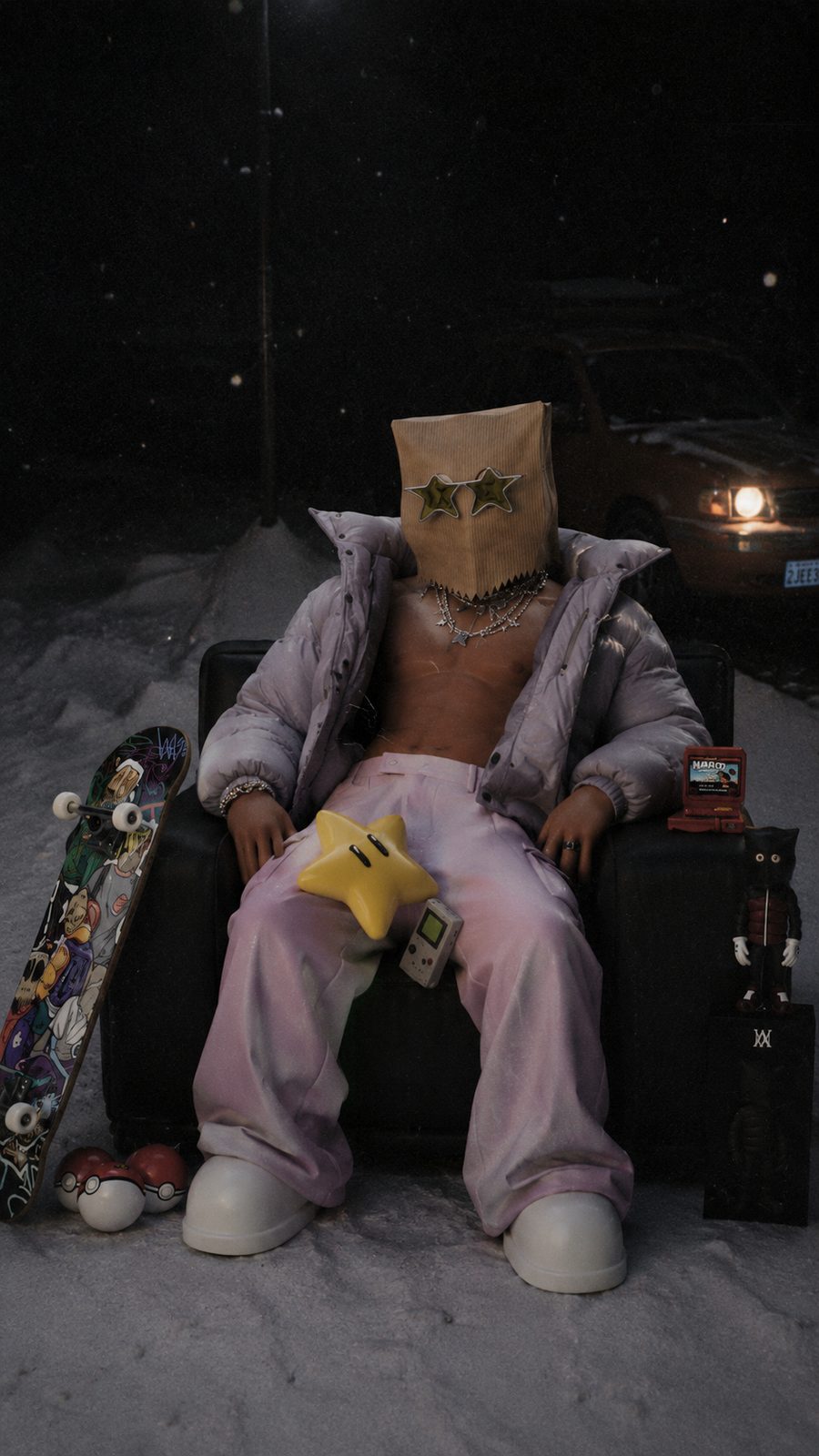 ASM paper-bag character with star-shaped glasses in a lilac puffer jacket and pink trousers, seated in an armchair in the snow at night beside a skateboard, toys and a parked car